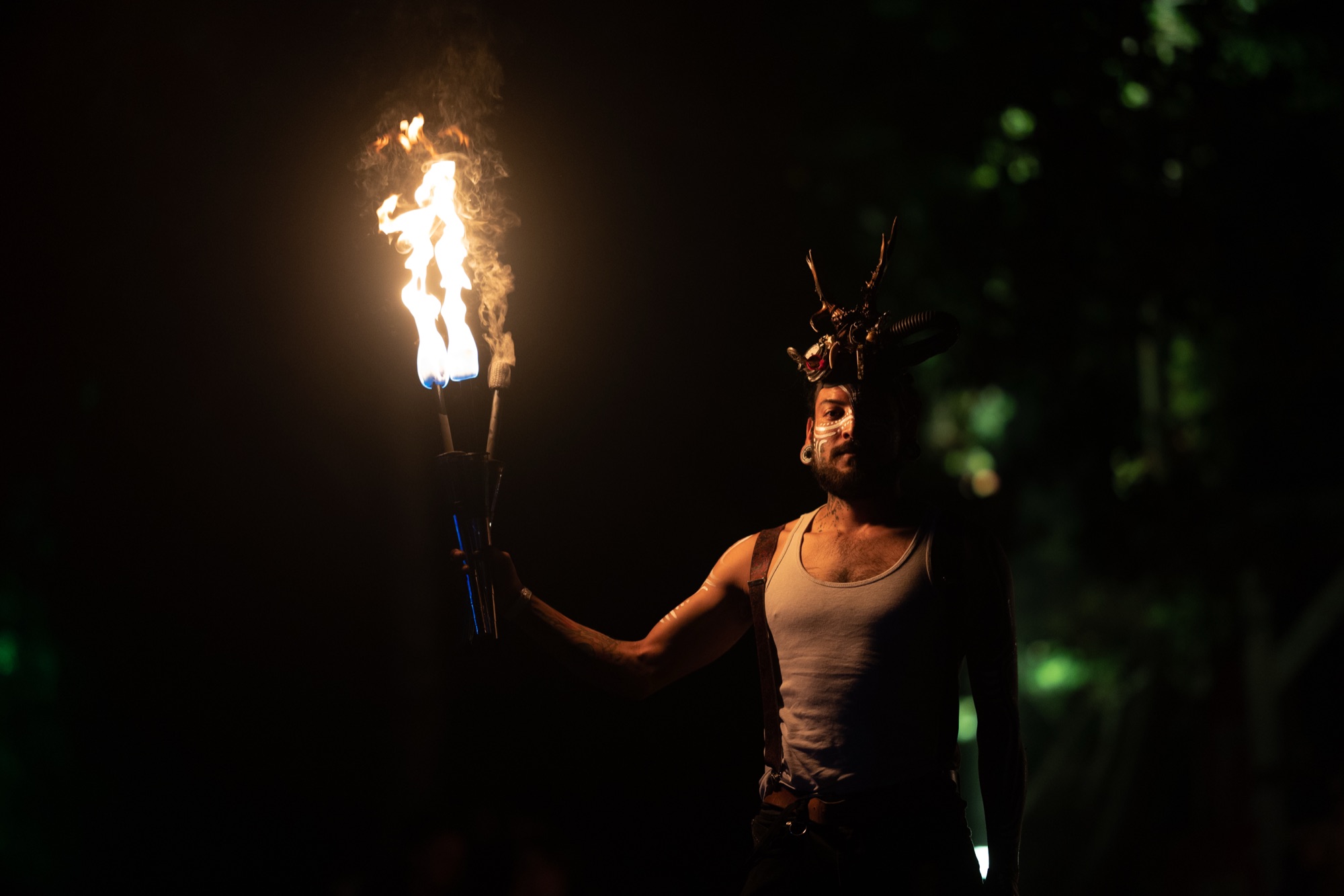 A performer with an antler headpiece holds a burning torch in total darkness
